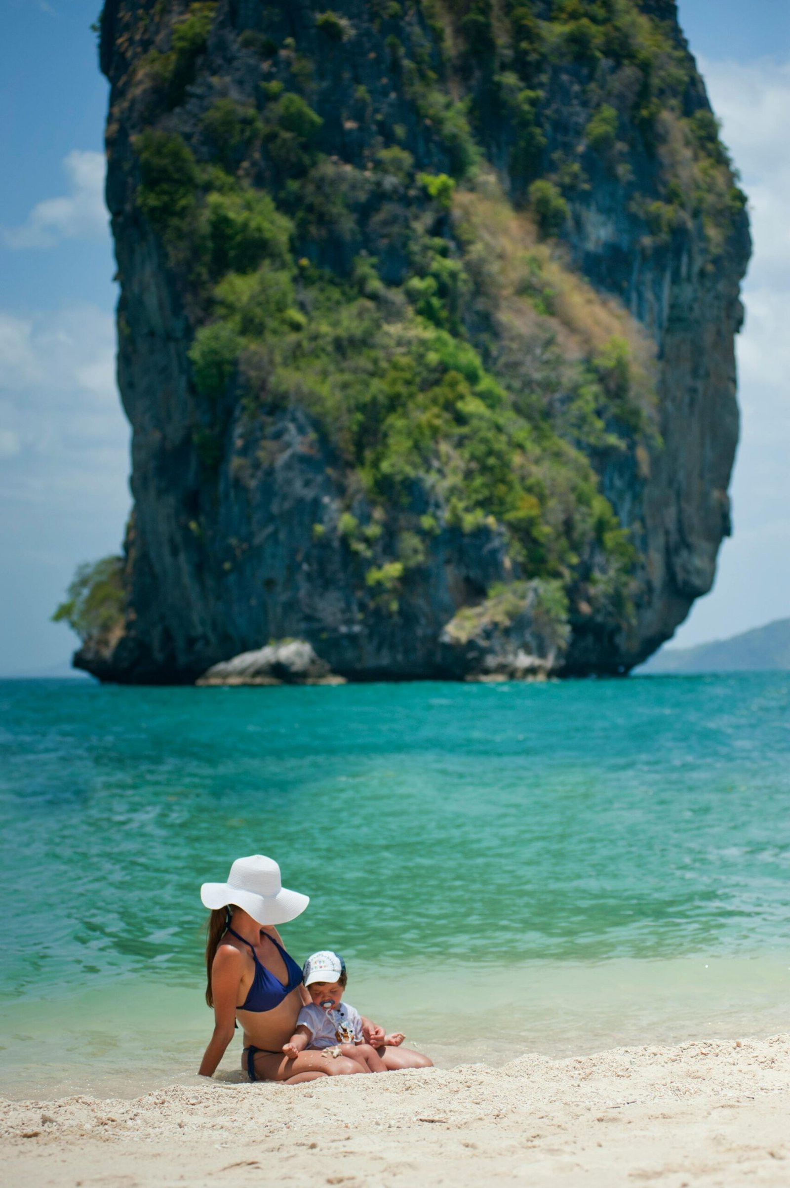 A mother and child relaxing on Ao Nang beach with a scenic limestone backdrop in Krabi, Thailand.